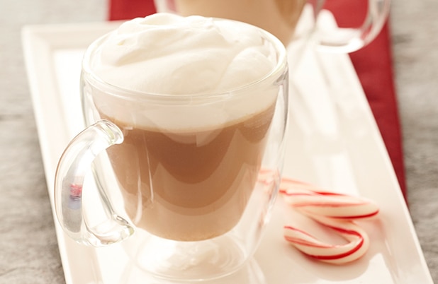 A frothy peppermint mocha in a tall glass with whipped cream and a candy cane.